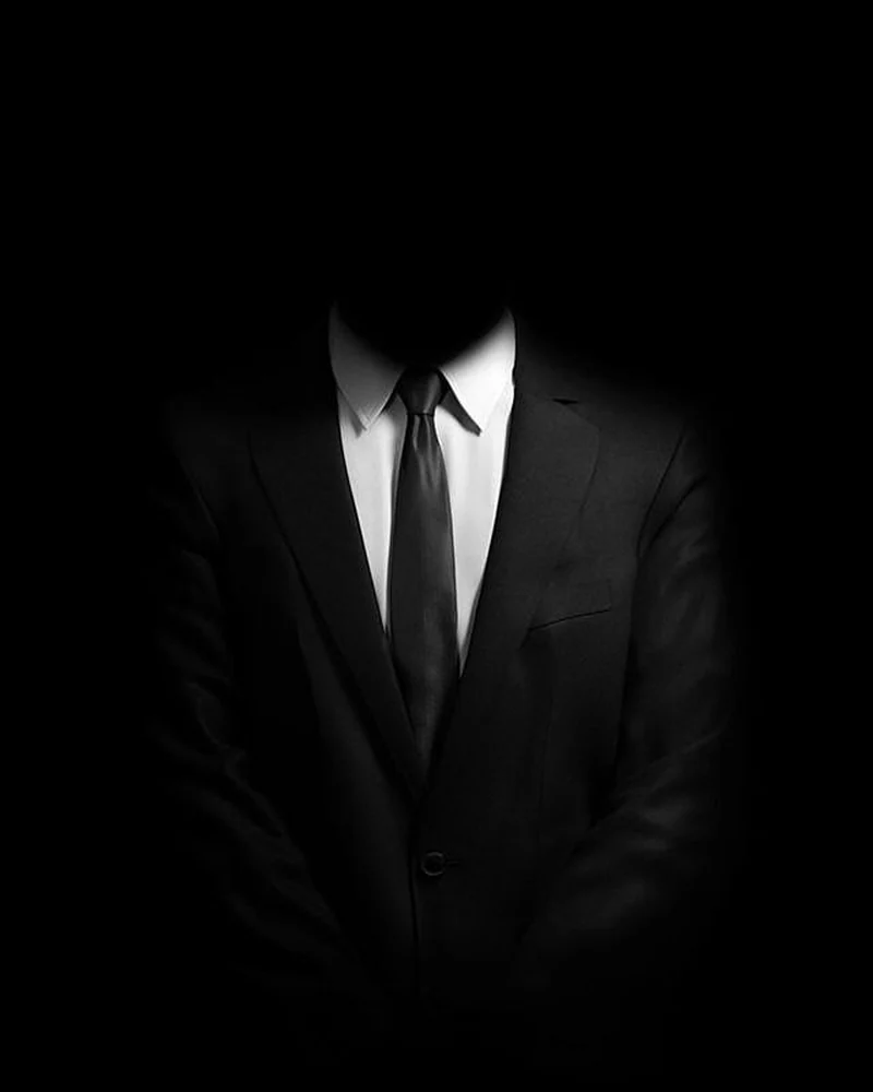 A figure in a dark suit, face unlit — the visual identity used for The Saint Dev
